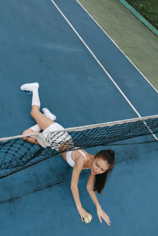 A young female tennis player struggles to reach a ball, demonstrating determination and athleticism on a vibrant blue tennis court, wearing sporty attire
