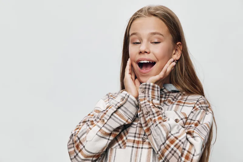 Girl with expression of surprise and joy with hands on cheeks in checkered shirt isolated on white background for emotion feeling and happiness concept.