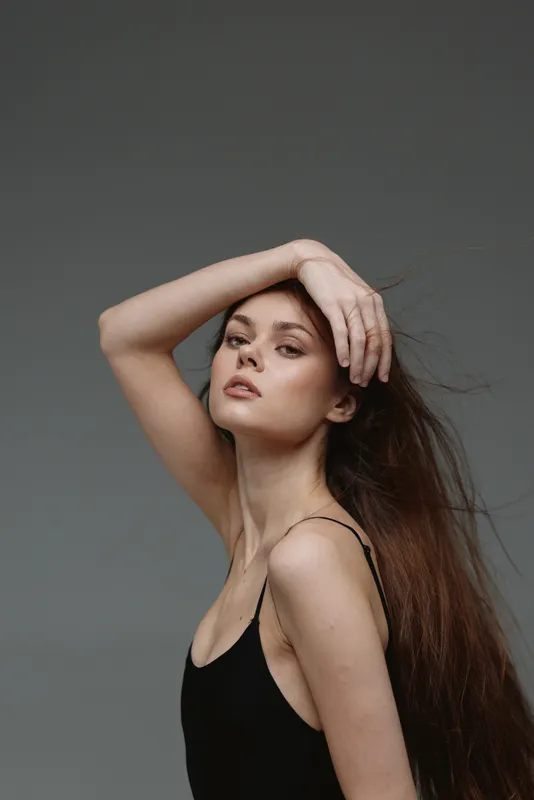 Elegant woman with long hair posing in black dress on gray background, confident expression and natural beauty