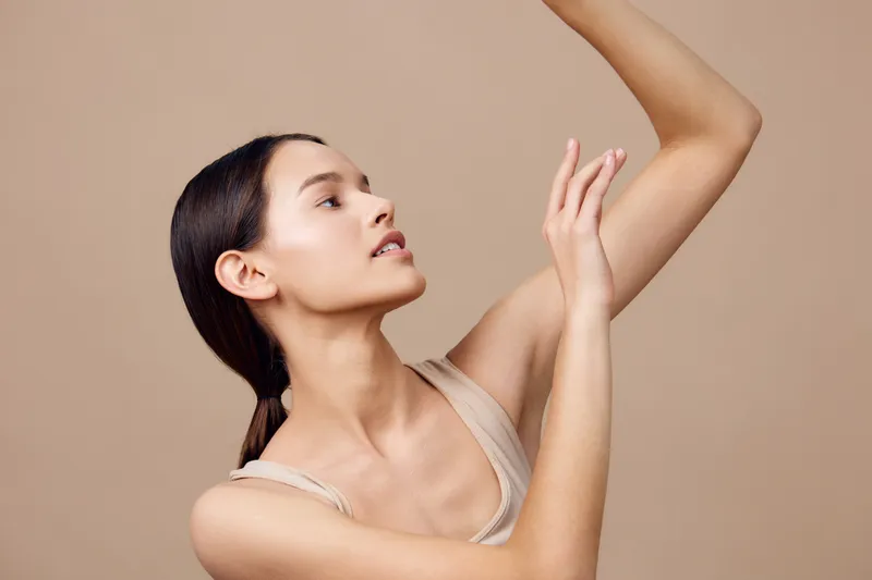 Elegant young woman with smooth skin posing gracefully against a neutral beige background, showcasing beauty and confidence in a minimalistic style