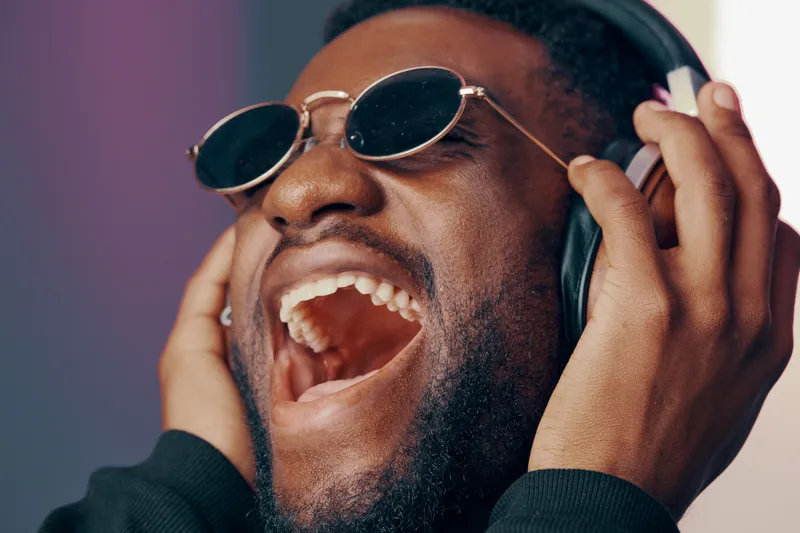 Happy young African American man enjoying music with headphones, expressing joy and excitement in a vibrant, modern setting, perfect for music related concepts