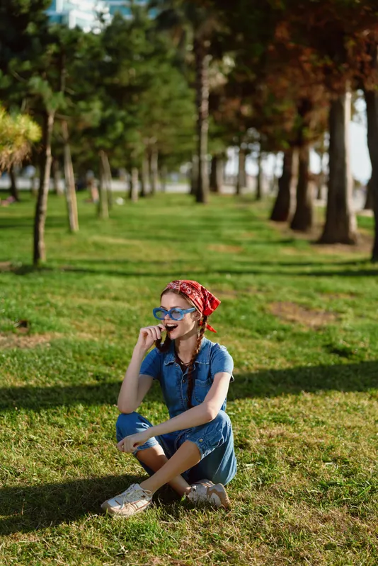 lifestyle woman in modern boho-western denim street style sits on grass enjoying sunny day with relaxed smile and colorful film color tones enhancing natural mood