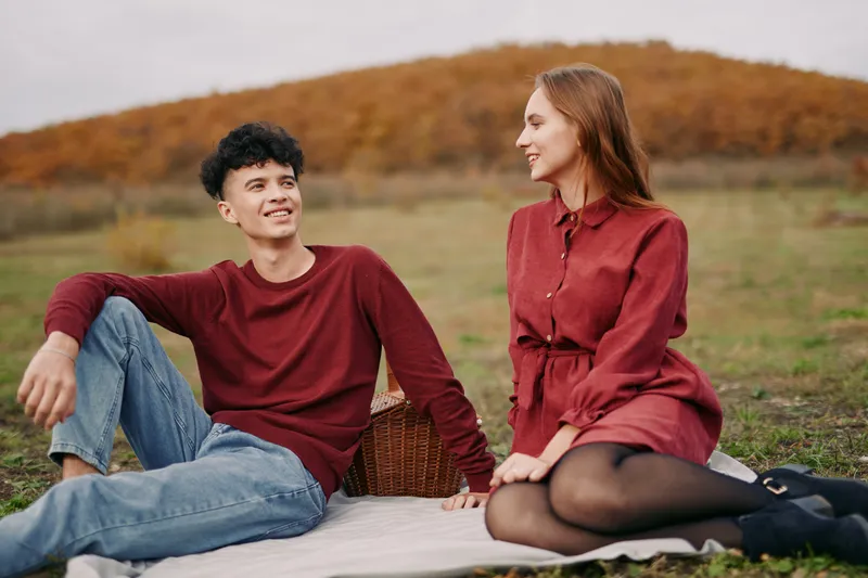 A candid scene emphasizes authenticity and credibility as a couple sits on a blanket in an autumn field, sharing a warm smile, quiet talk, and genuine connection.
