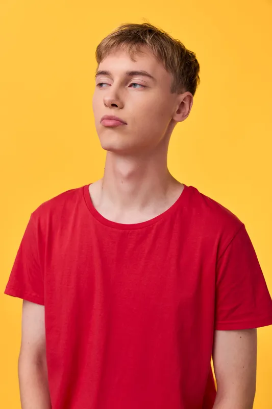 Young man wearing a red shirt against a vibrant yellow background in a studio setting, casual pose with distant gaze, fashion and lifestyle concept for a modern mood image