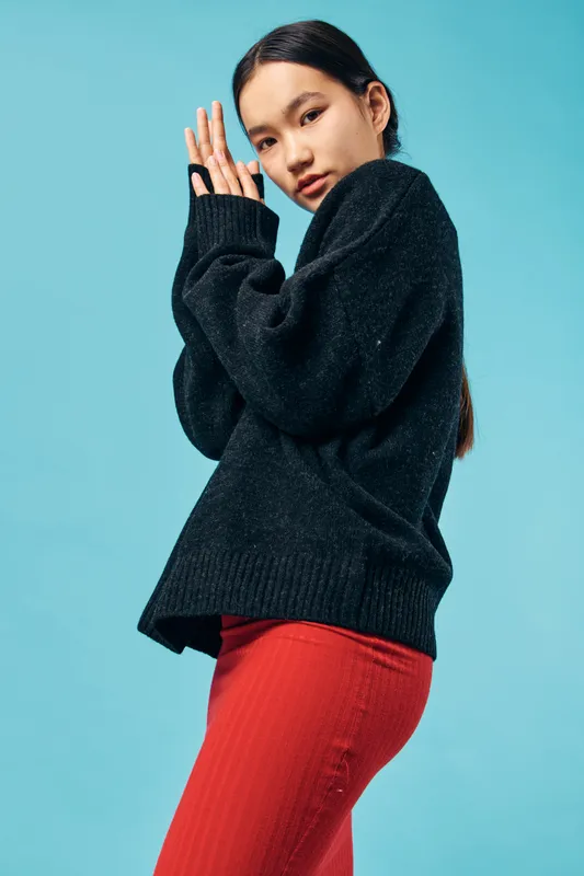 Young woman posing in black sweater and red pants on blue background for fashion portrait with casual style clothing and modern look in studio photography with natural expression.