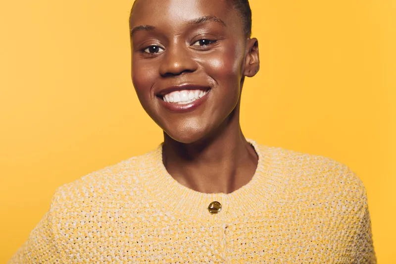 Smiling African woman with dark skin wearing a yellow sweater on a yellow background. Portrait of confident black female model with natural makeup and positive expression. Studio shot.