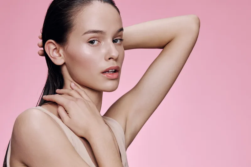 Young model with elegant pose and natural makeup against a soft pink background, showcasing beauty and femininity in a fashion forward concept