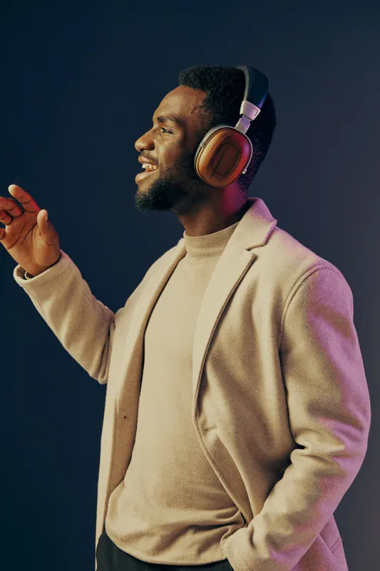 Joyful man wearing headphones in a stylish outfit, smiling and enjoying music against a colorful background, reflecting a modern lifestyle