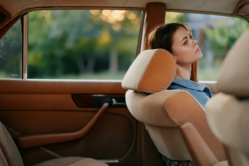 Thoughtful young woman resting in a vintage car, showcasing a contemplative expression with a blurred natural background highlighting summer vibes.