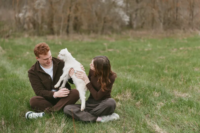 goat kid couple people outdoors meadow grass animal interaction laughter sunshine nature contact gentle playful field happiness portrait lifestyle balance friendship warmth carefree rustic pasture