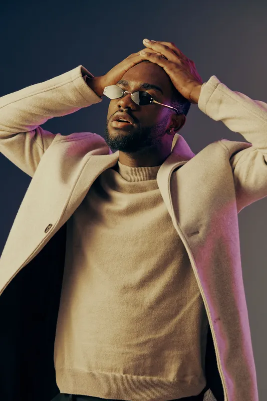 Stylish young man expressing frustration in a modern setting, wearing a beige sweater and coat, perfect for emotional portraits and lifestyle content