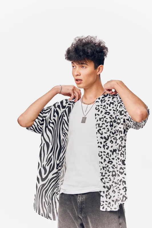Young man with curly hair wearing a half zebra, half leopard print shirt and white t-shirt, posing against a plain white background with a casual expression.