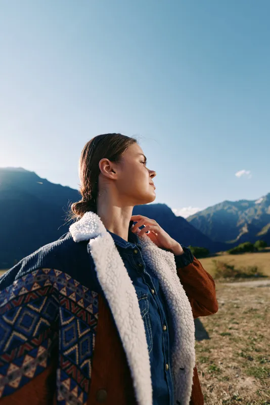 Woman portrait in the mountains hiking outdoors with backpack and jacket, enjoying sunlight and nature, travel adventure and serene landscape for leisure and exploration moments.
