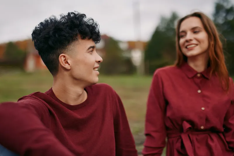 A candid portrait of a young couple sharing a genuine moment outdoors, capturing natural expressions and authentic connection with relaxed posture and soft seasonal background.
