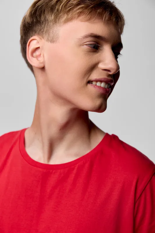 Young man in a red shirt looking away with a gentle smile, casual style, studio lighting, clean background, fashion and daily wear concept, relaxed and approachable vibe