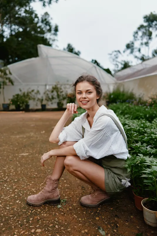 Young woman in casual fashion, wearing a white shirt and green shorts, smiling outdoors in a garden setting, showcasing a natural and relaxed lifestyle