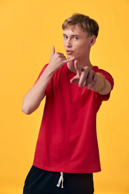Youthful figure in a red shirt performs a call gesture against a bright yellow background, highlighting communication, confidence, and friendly, dynamic pose