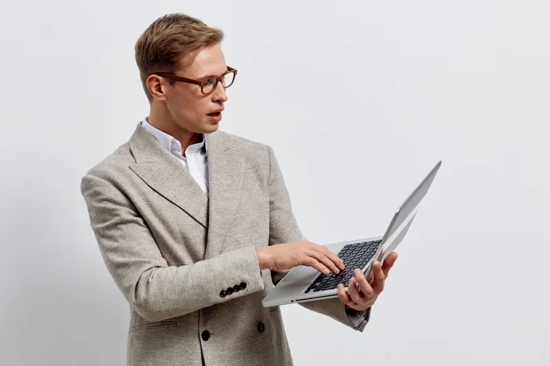 Professional young man in beige blazer working on laptop computer isolated on plain white background studio portrait. Business casual concept