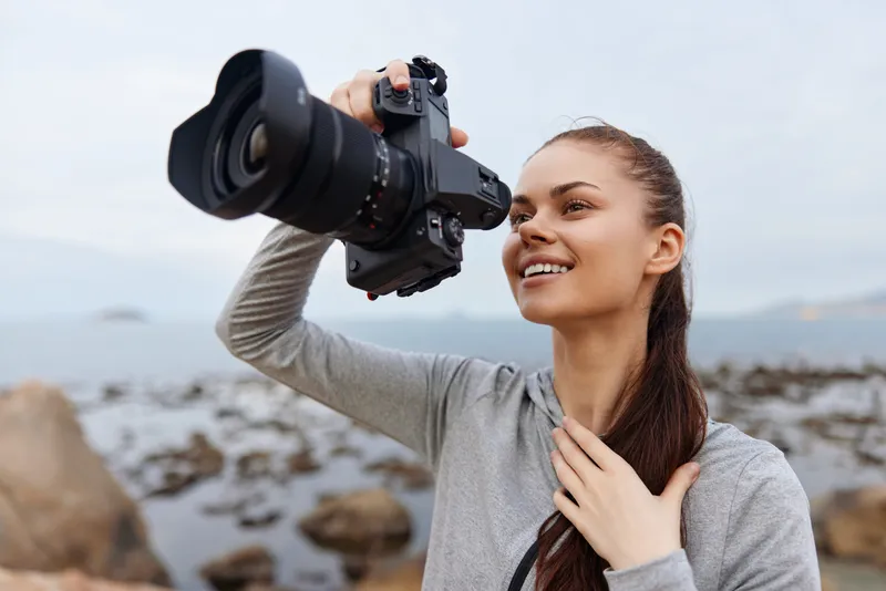 Young woman taking photographs by the seaside, showcasing joy and passion for photography with a professional camera, wearing casual sportswear