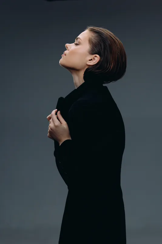 Profile of a thoughtful woman in black coat against dark background, contemplative mood, winter season, elegant style