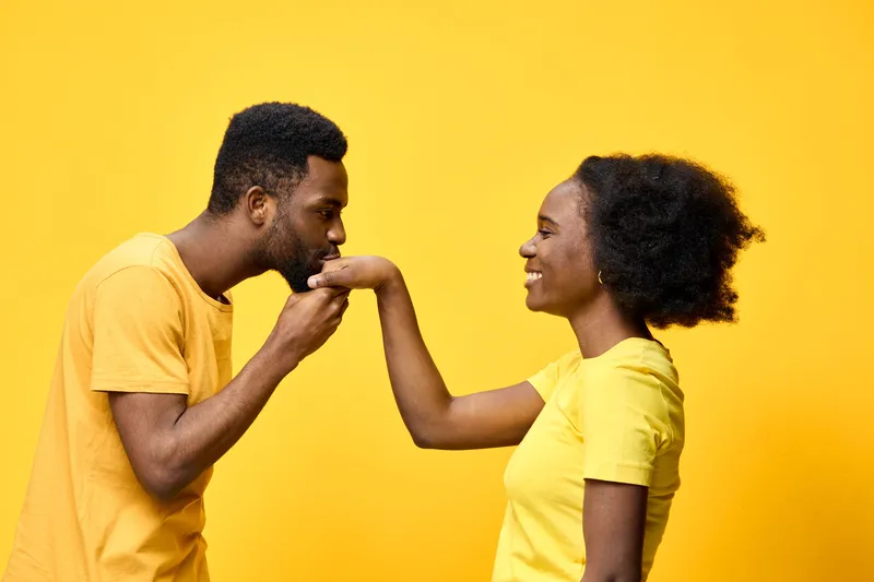 A joyful African couple wearing matching yellow t shirts enjoys a tender moment together, showcasing love and connection against a bright yellow background