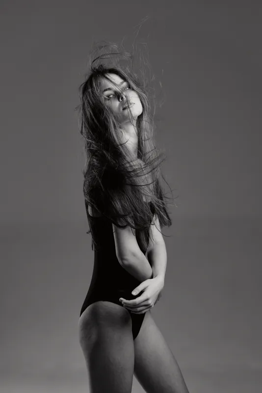 Black and white portrait of a woman with flowing hair and thoughtful expression in minimalistic studio setting.