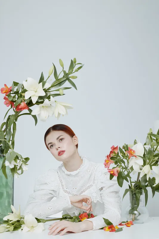 Elegant woman with flowers in a minimalist setting, wearing a white dress, expressing serenity, perfect for themes of beauty and spring
