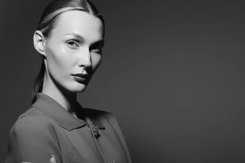 Young caucasian woman with pale skin and slicked hair looks confidently in monochrome studio portrait.