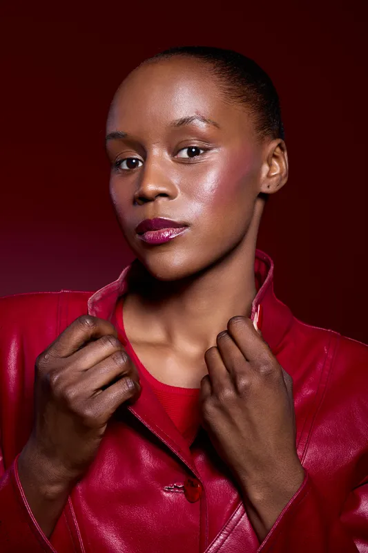 Confident black woman with dark skin wears red leather jacket and red top. Studio portrait on dark red background. Concept for fashion, beauty, empowerment, and style.