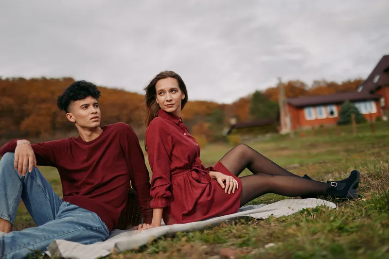 Young couple lounging on a picnic blanket in a countryside field, photographed with authenticity and credibility in a candid, natural composition that highlights relaxed connection and genuine