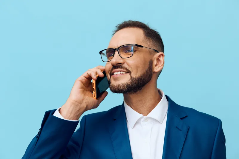 A professional businessman stands against a bright colored background, isolated and polished, as he talks on a phone with a confident, focused mood and clear intent.
