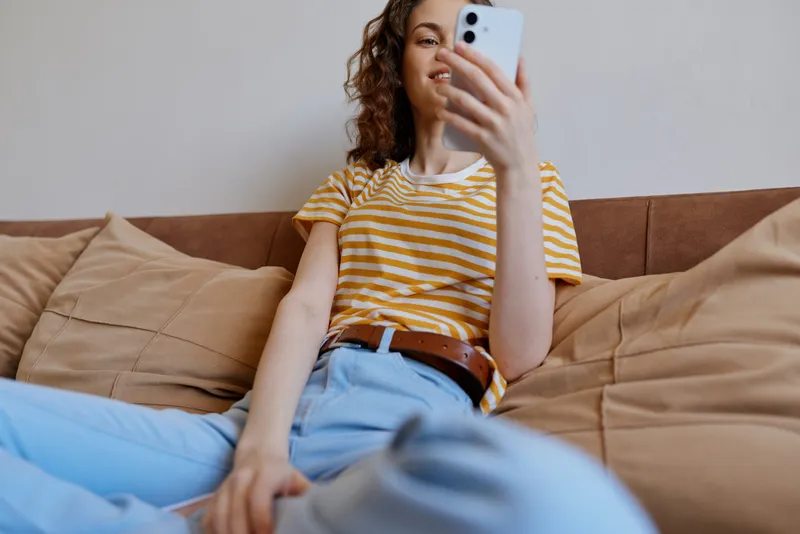Woman relaxing at home takes a casual selfie on a couch with smartphone, capturing a relaxed lifestyle and interior comfort in a modern setting.