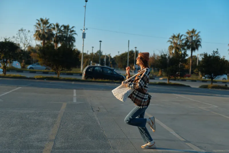 Woman running across empty parking lot at golden hour, candid lifestyle moment with joy and authenticity, mindful living vibe and emotional storytelling in urban sunset light.