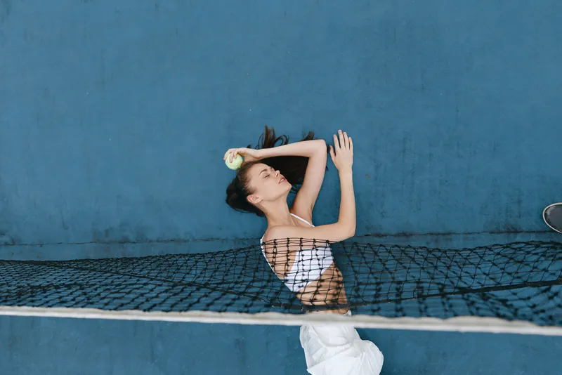 Energetic young woman playing tennis, wearing a sporty outfit, with emotions of concentration and joy, on a vibrant blue court background