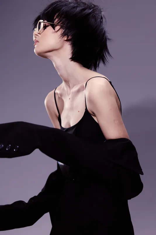 Stylish woman with short black hair in black outfit and glasses posing against soft purple background