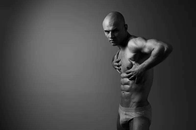 Black and white image of a muscular man showcasing a powerful pose, capturing strength and confidence in a dramatic lighting setup.