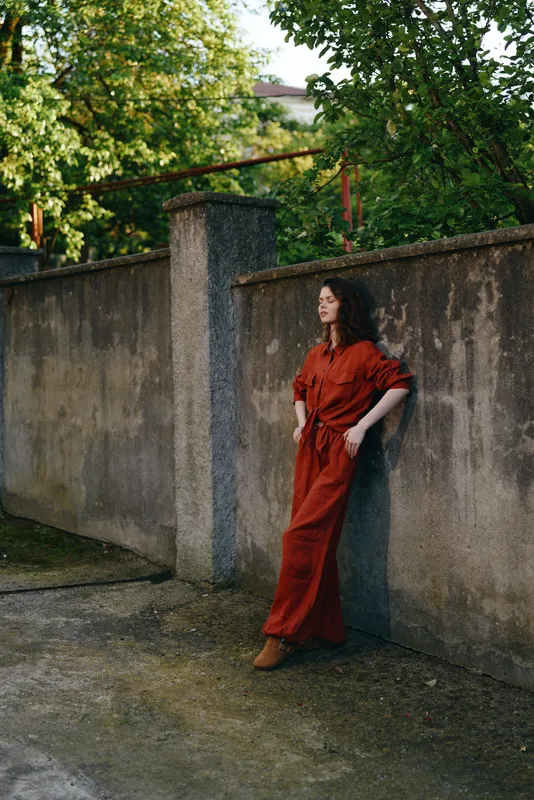 A woman in a red dress leans against a concrete wall in an outdoor setting, capturing a casual, contemplative moment. Lifestyle concept for style and solitude
