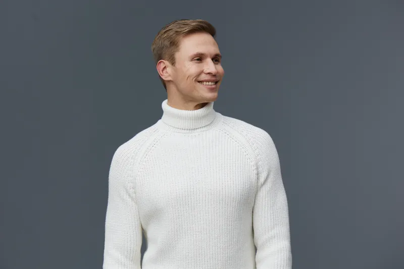 smiling man wearing white turtleneck sweater look aside studio portrait casual outfit cheerful expression digital detox concept