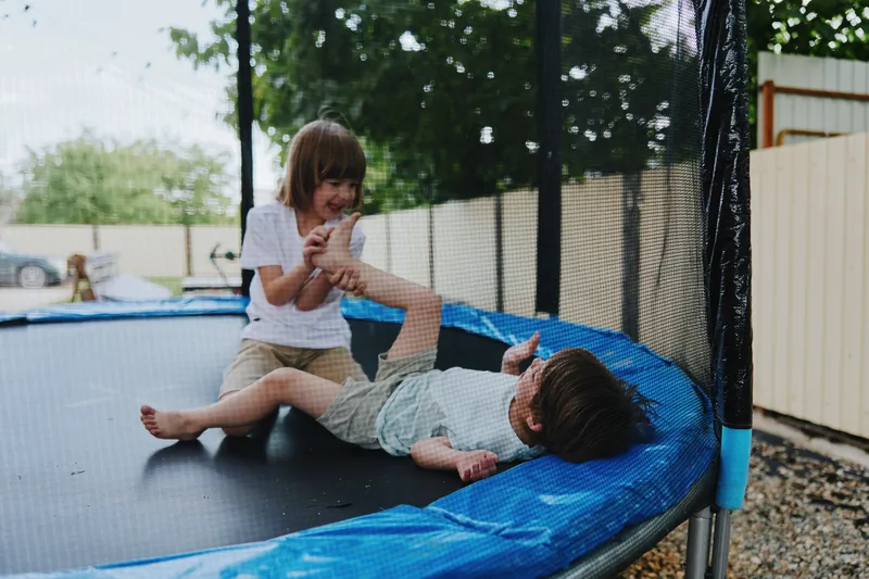 Playful children enjoying a trampoline, laughing joyfully in a sunny backyard, surrounded by greenery and a bright atmosphere, embracing fun and adventure.