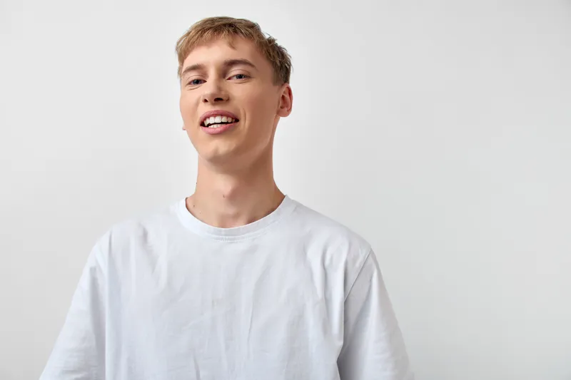 Smiling man wearing a white t shirt showcases casual style and a happy expression, lit with studio light for a bright, approachable look ideal for lifestyle, fashion, and marketing campaigns