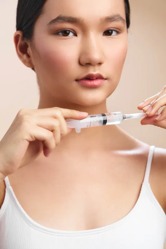 Asian woman calmly prepares a syringe in a clean clinical setting. She focuses on the task, conveying care, safety, and professional precision during medical procedures.