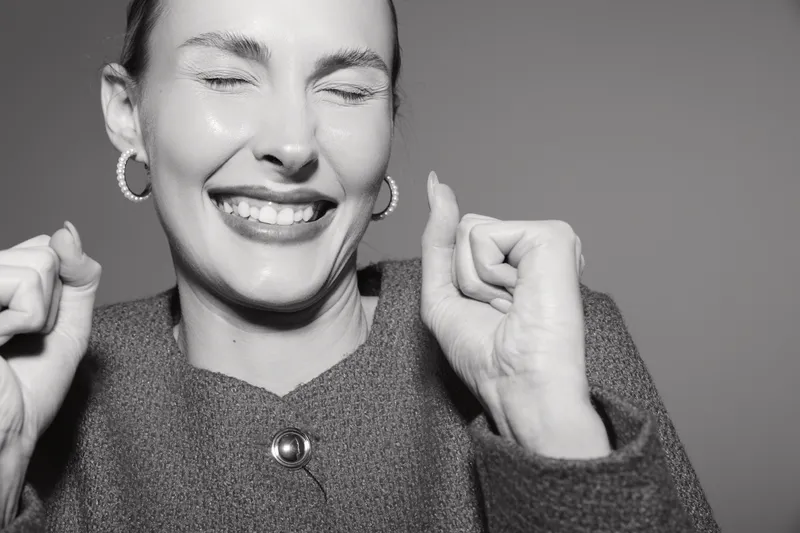 Happy Caucasian woman with light skin smiling with eyes closed and raised hands. Studio portrait in black and white photography.