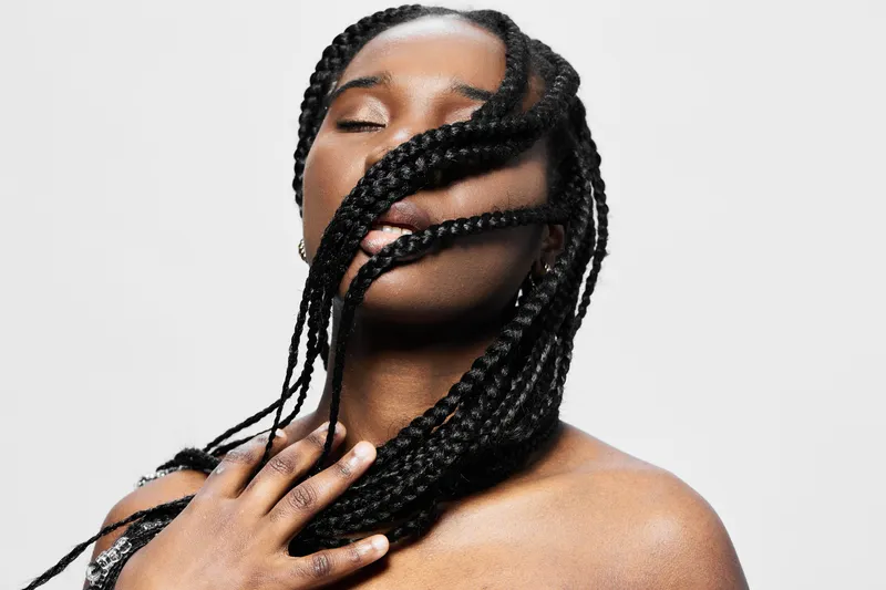 Beautiful young woman with braided hair, closed eyes, and confident expression, highlighting beauty and elegance on a minimalist white background