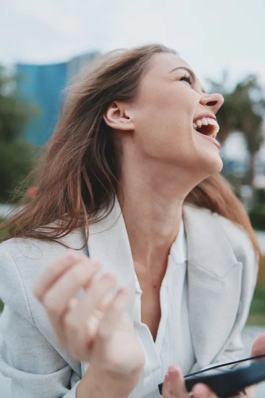 Happy woman with light brown hair laughing outdoors in casual business attire during daytime city background financial crisis joy emotion