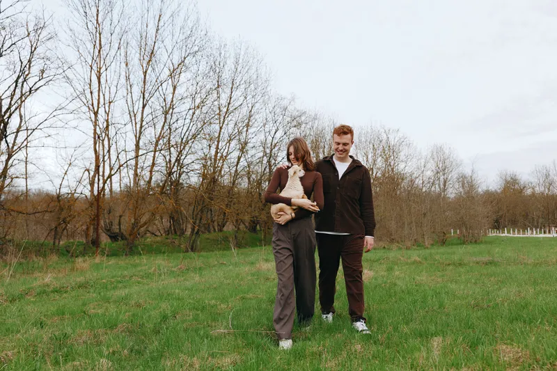 Outdoor family scene with a goat kid, a relaxed walk in a sunlit field, casual clothing, gentle breeze, natural colors, a candid moment of togetherness amid open nature