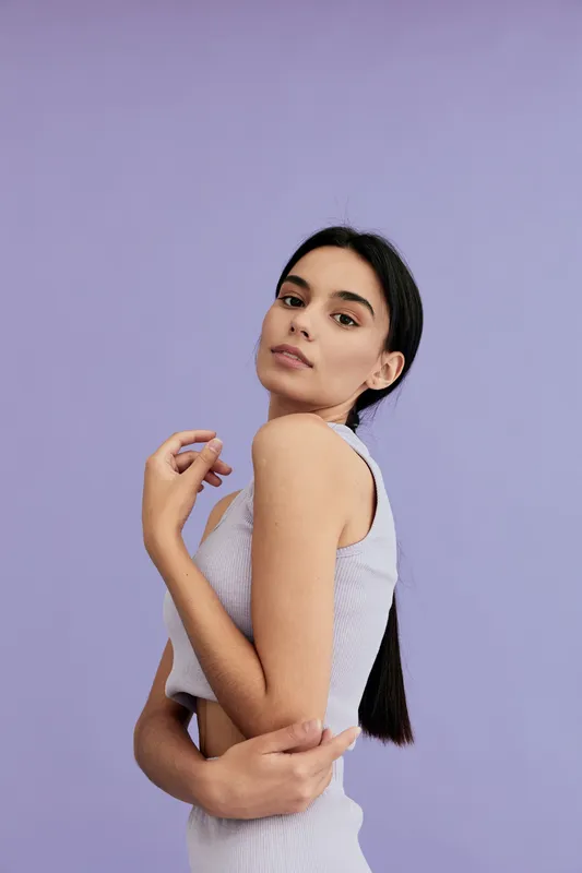 young woman posing with calm expression in sleeveless light purple top against soft lavender background, showcasing natural beauty and minimalistic style