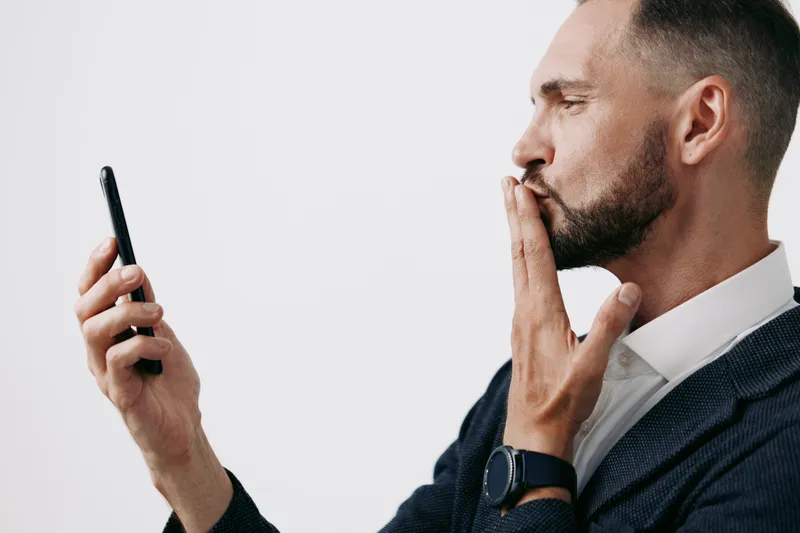 A professional man in a suit uses a mobile device, displaying focus and contemplation against an isolated colored background, suitable for business themes.