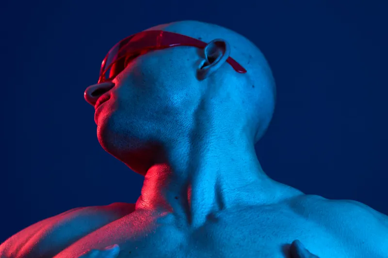 Bold man with stylish sunglasses under dramatic blue and red lighting, showcasing confidence and strength, perfect for concepts of style and modernity.