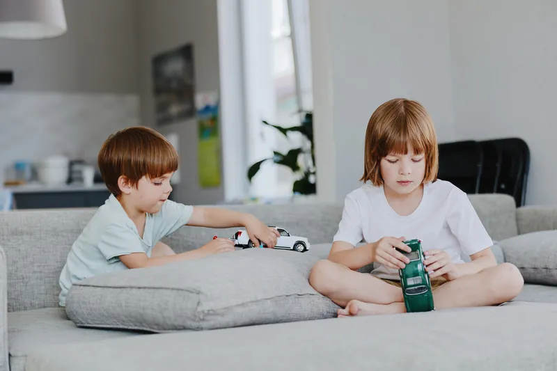 Two children playing with toy cars in a cozy living room, showcasing a playful and joyful atmosphere, perfect for family-related content.