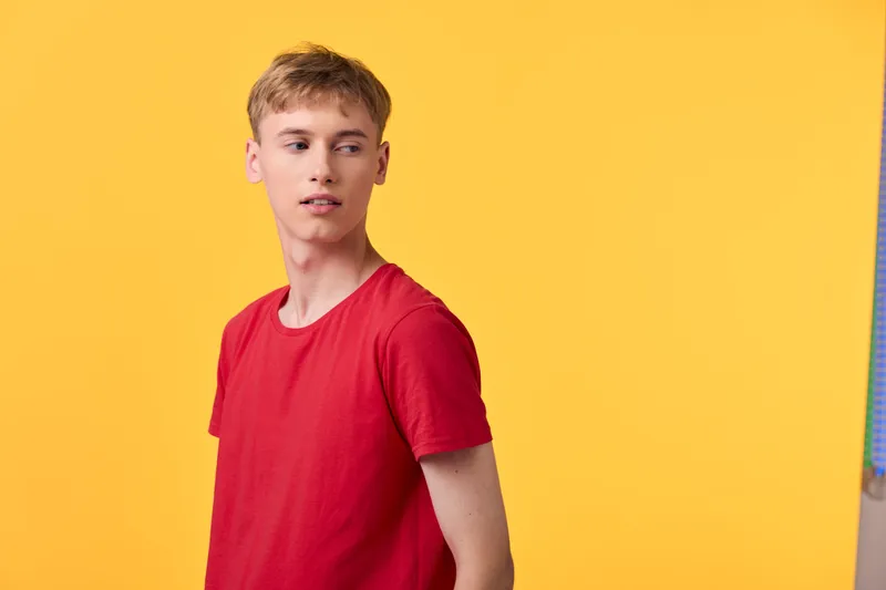 Man wearing a red shirt against a bright yellow backdrop, casual pose and relaxed expression, fashion and lifestyle photography with bold color contrast and vibrant mood